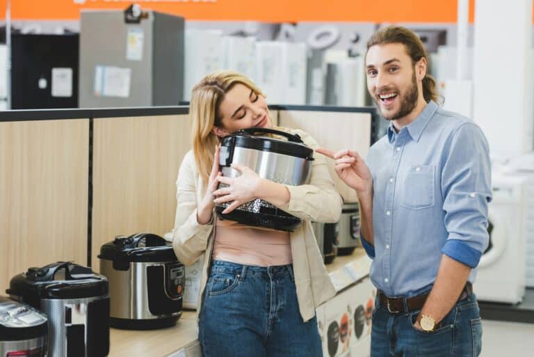 smiling consultant pointing with finger at woman with slow cooker in home appliance store