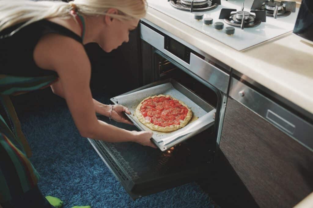 Femme mettant une pizza à réchauffer dans on four à micro-ondes encastrable