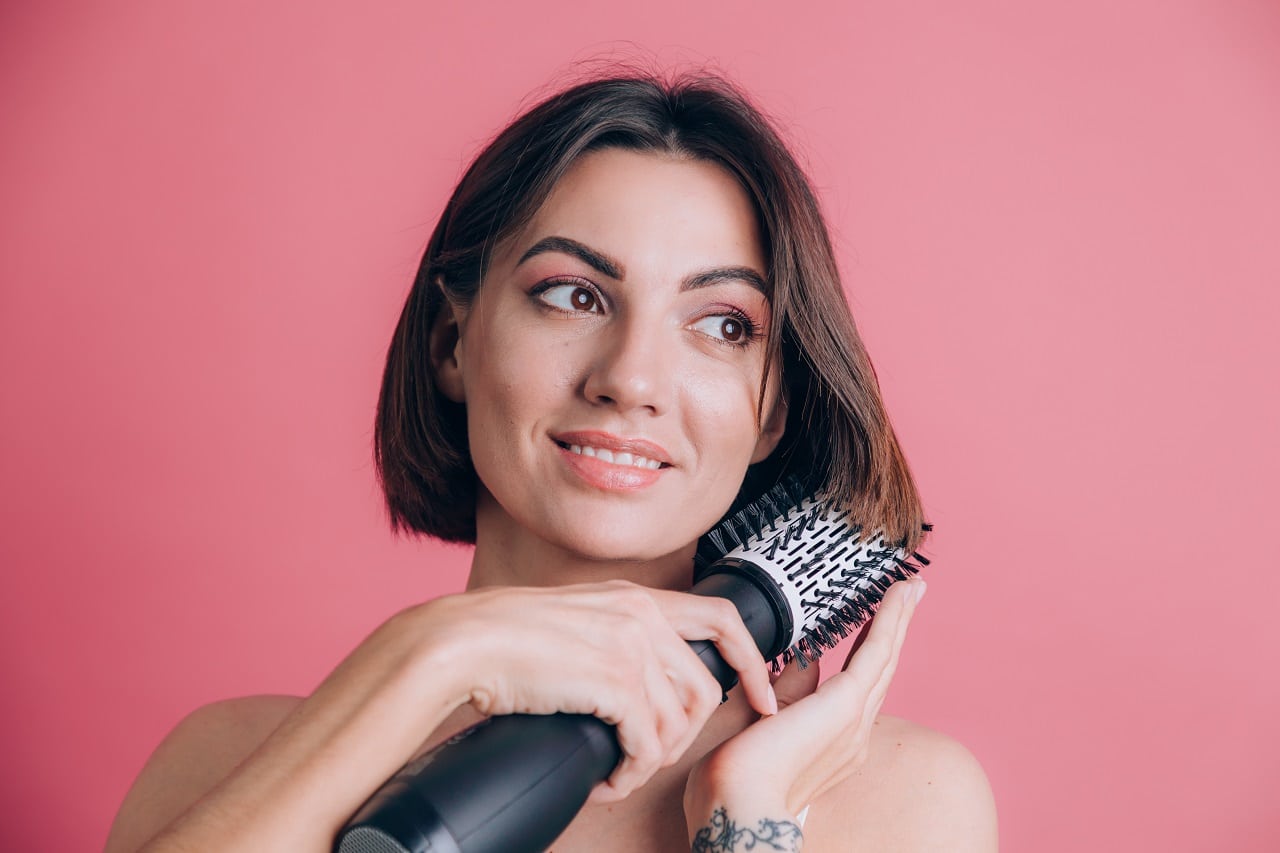 Une jeune femme brune se lissant les cheveux avec une brosse soufflante rotative