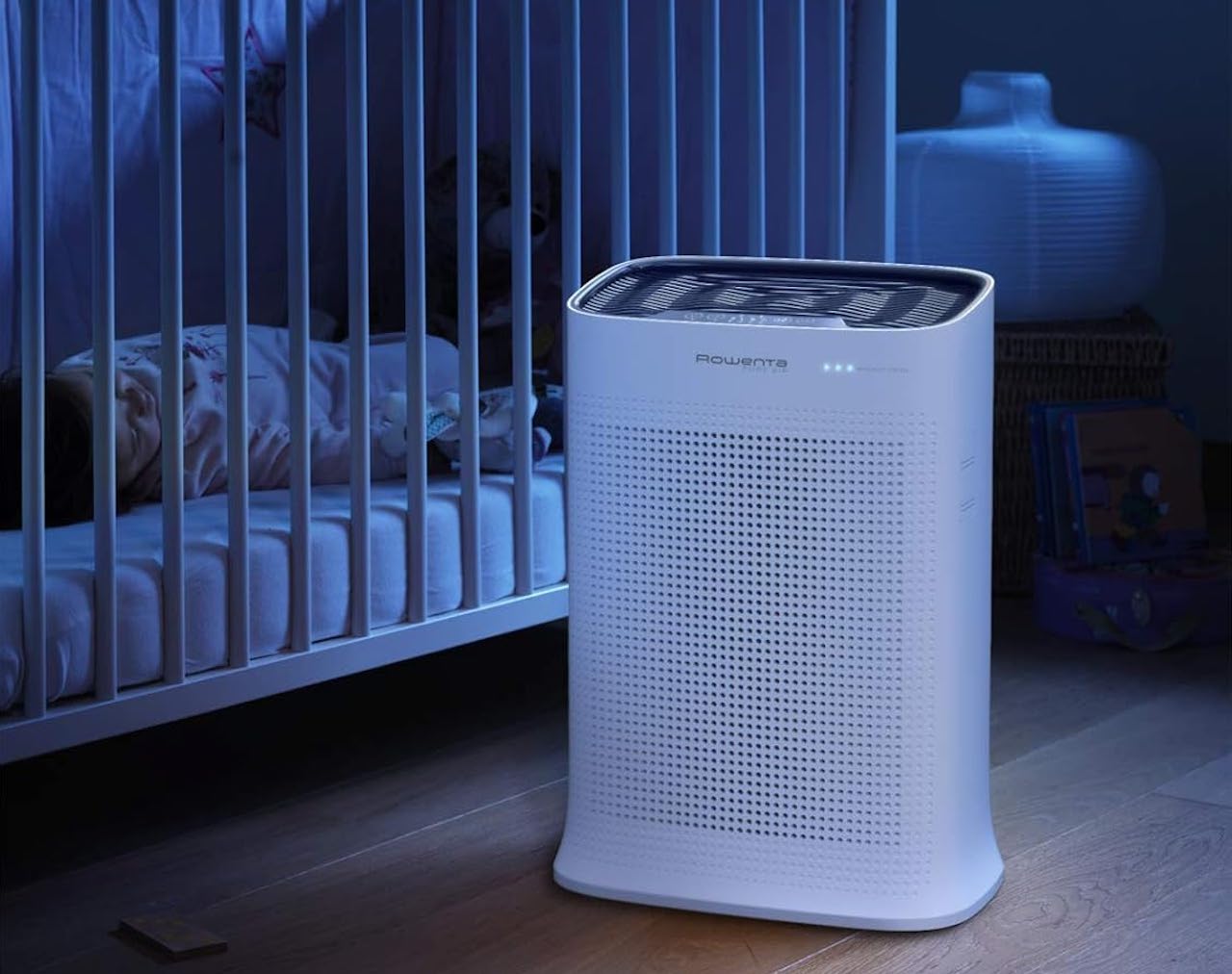 Un purificateur d'air de la marque Rowenta. Il est disposé dans une chambre de bébé, près du berceau où l'enfant dort.