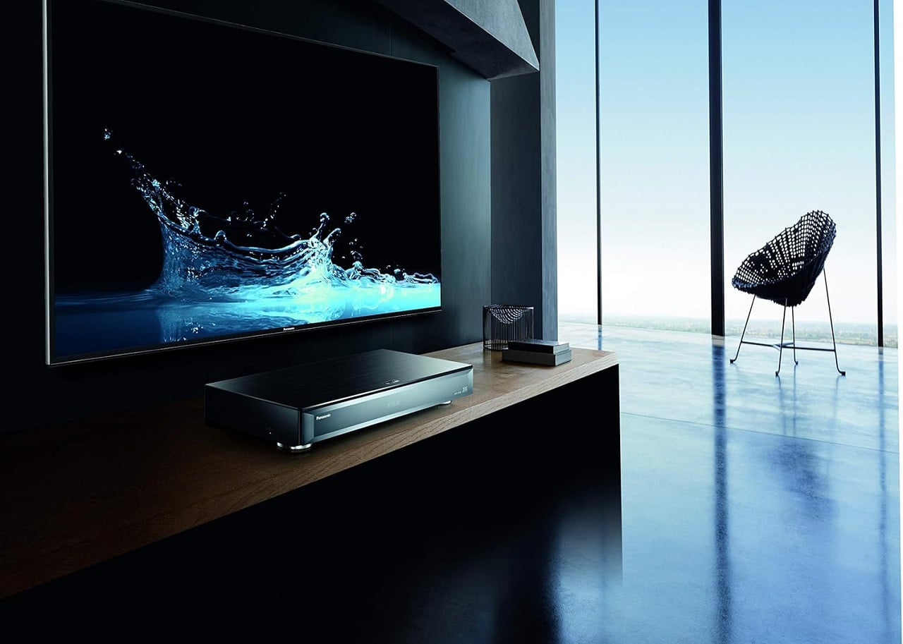 Une installation home cinéma dans un salon avec sur un meuble TV un lecteur blu-ray 4K Panasonic et au mur un écran plat qui diffuse une image 4K magnifique