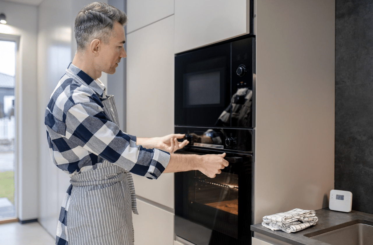 Un homme dans un cuisine qui règle le four pour préparer un plat.