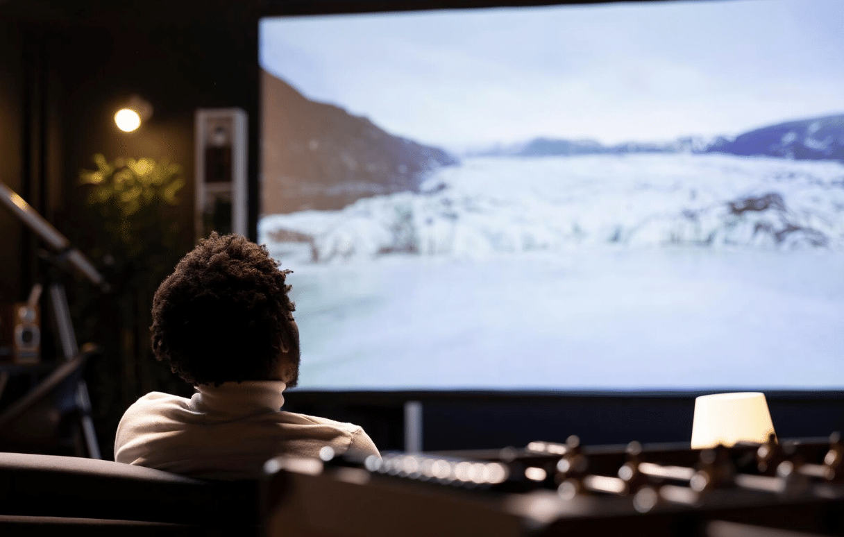 Un homme assis devant un écran de vidéoprojecteur. Il regarde un film.
