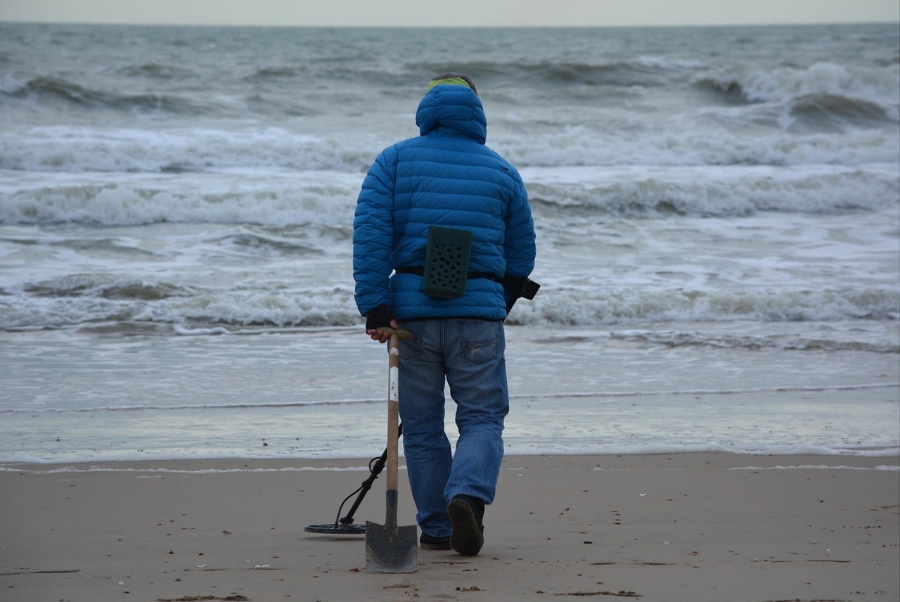 Un homme munit d'une pelle et d'un détecteur de métaux sur une plage