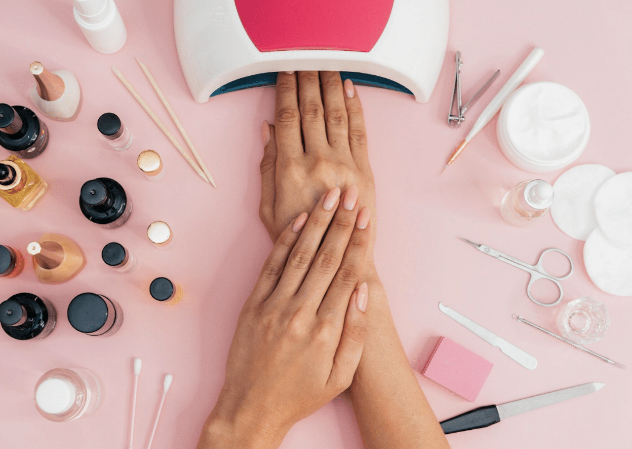 Une vue aérienne d'un plan de travail pour faire une manucure : il y a des vernis à ongle, une lampe UV, une lime à ongle, etc..