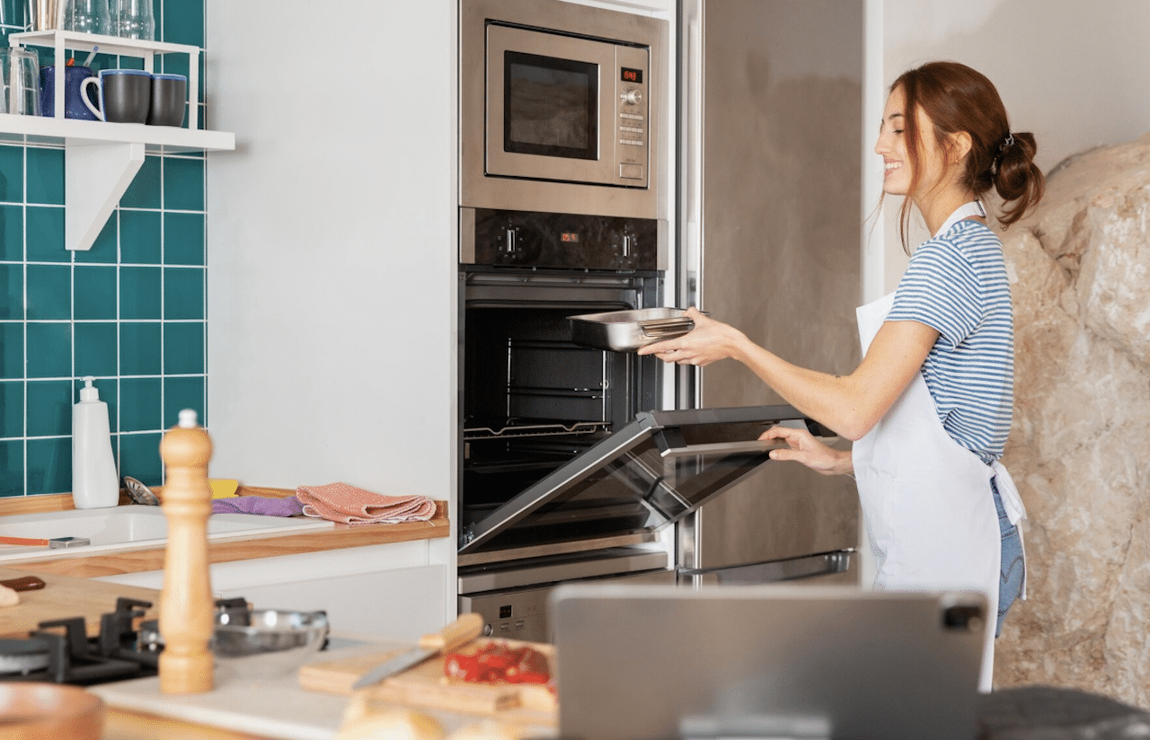 Une femme cuisinant dans sa cuisine. Elle ouvre son four encastrable pour y mettre un plat.