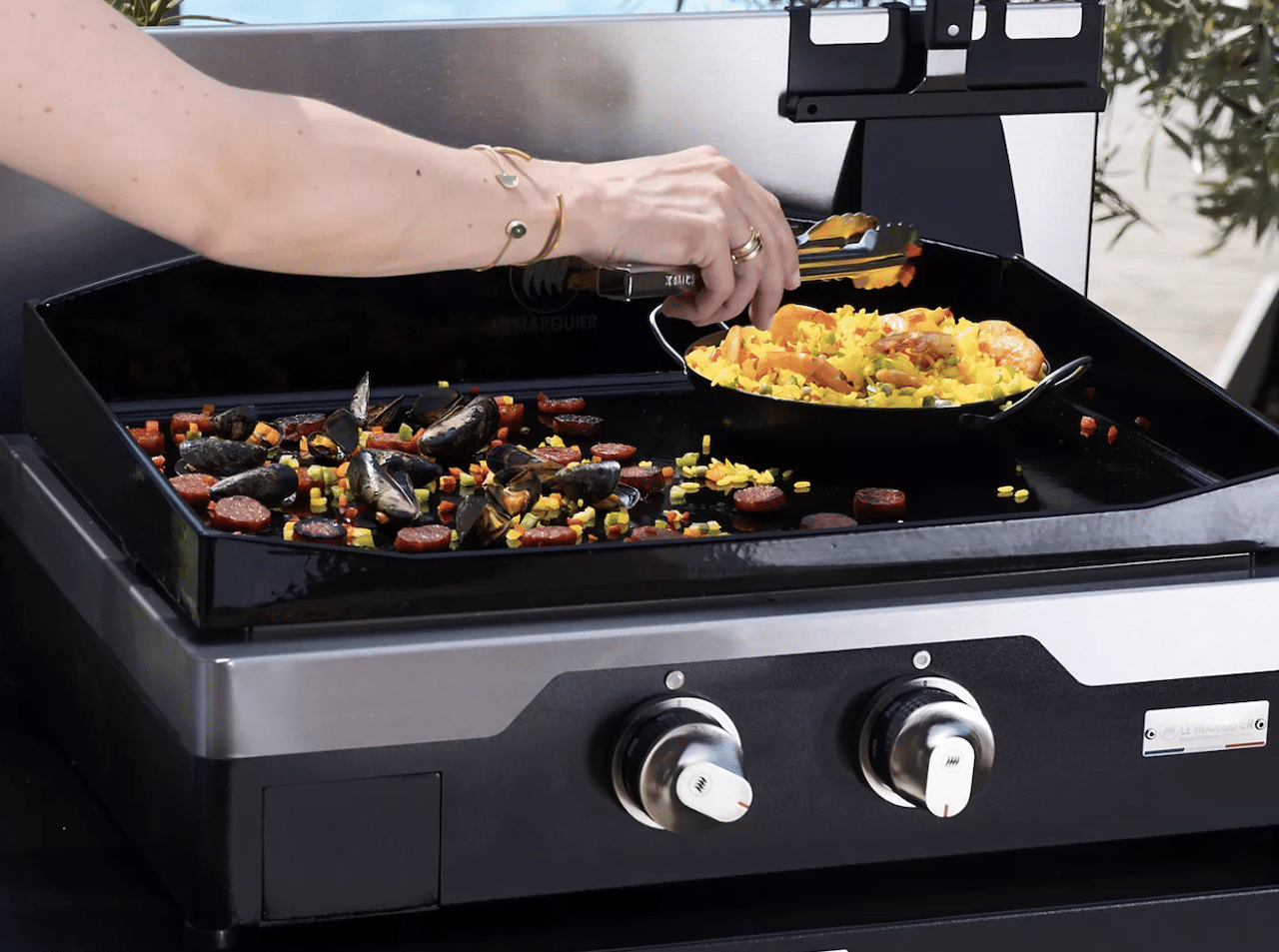 Une femme qui péprare une paella sur une plancha de la marque Le Marquier.