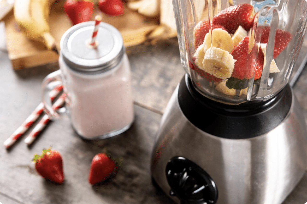 Un blender avec des fruits dedans, et un smoothie à côté.
