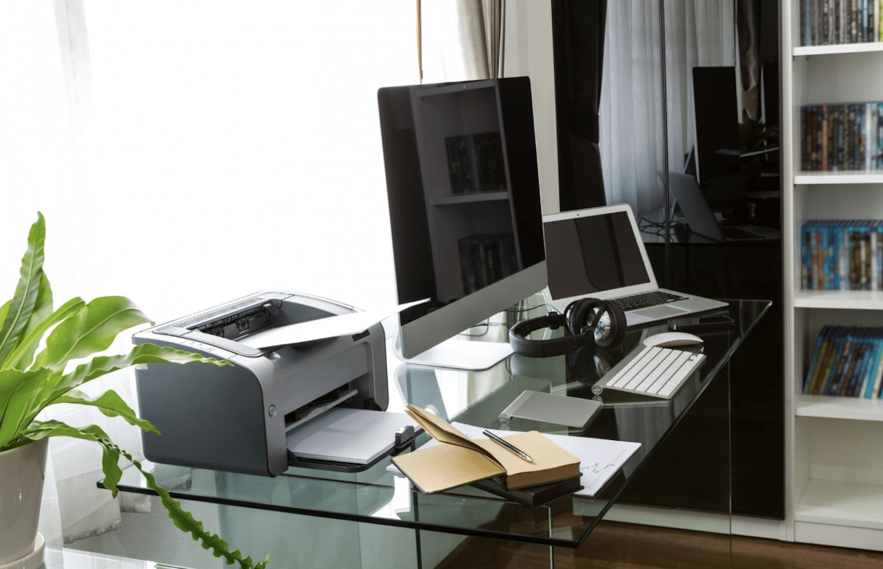 Un bureau en verre avec un ordinateur et une imprimante.
