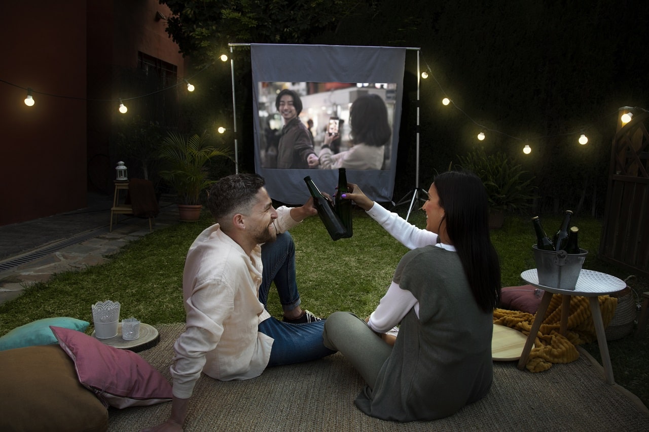 Un couple dinant sur l'herbe en visionnant un film grâce à un videoprojecteur