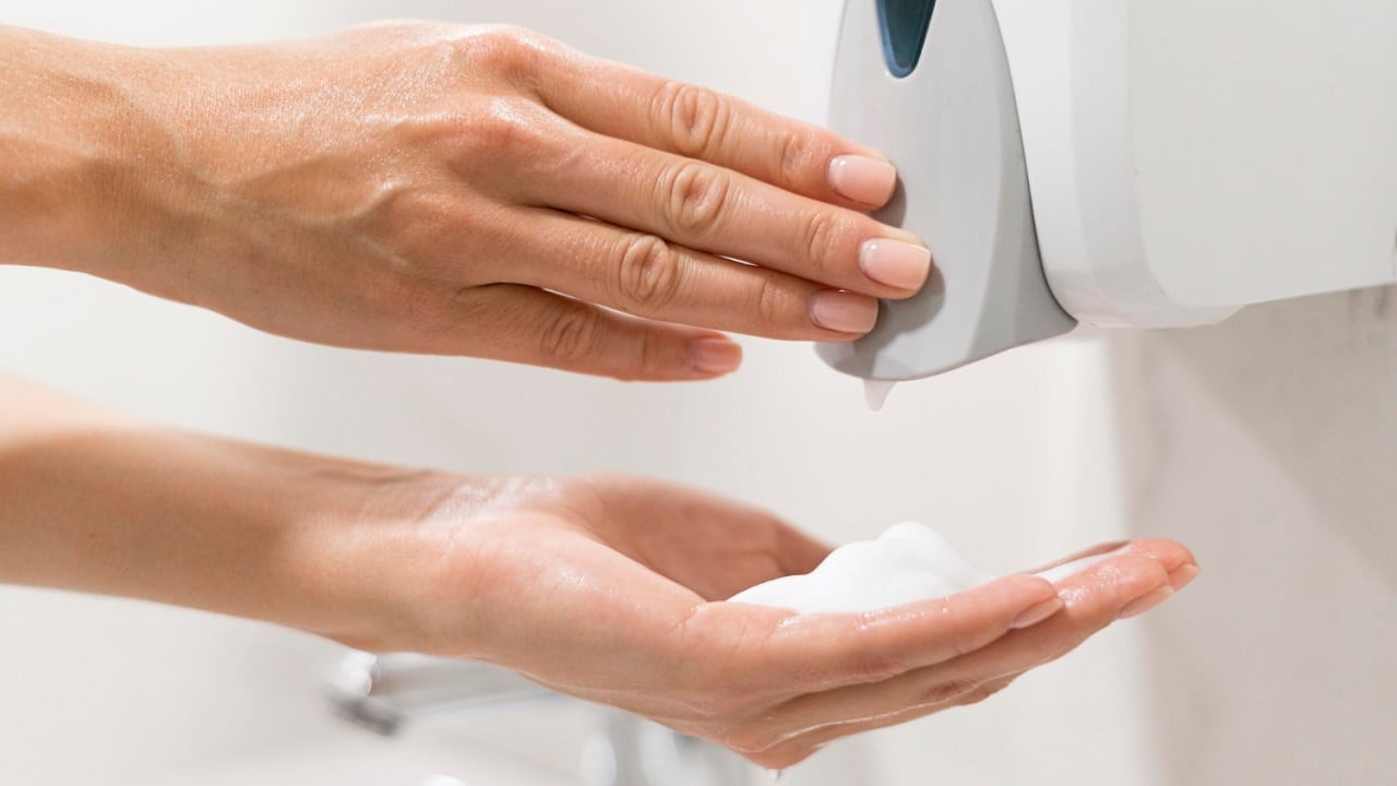 Une personne se lavant les mains en utilisant un distributeur automatique de savon fixé au mur