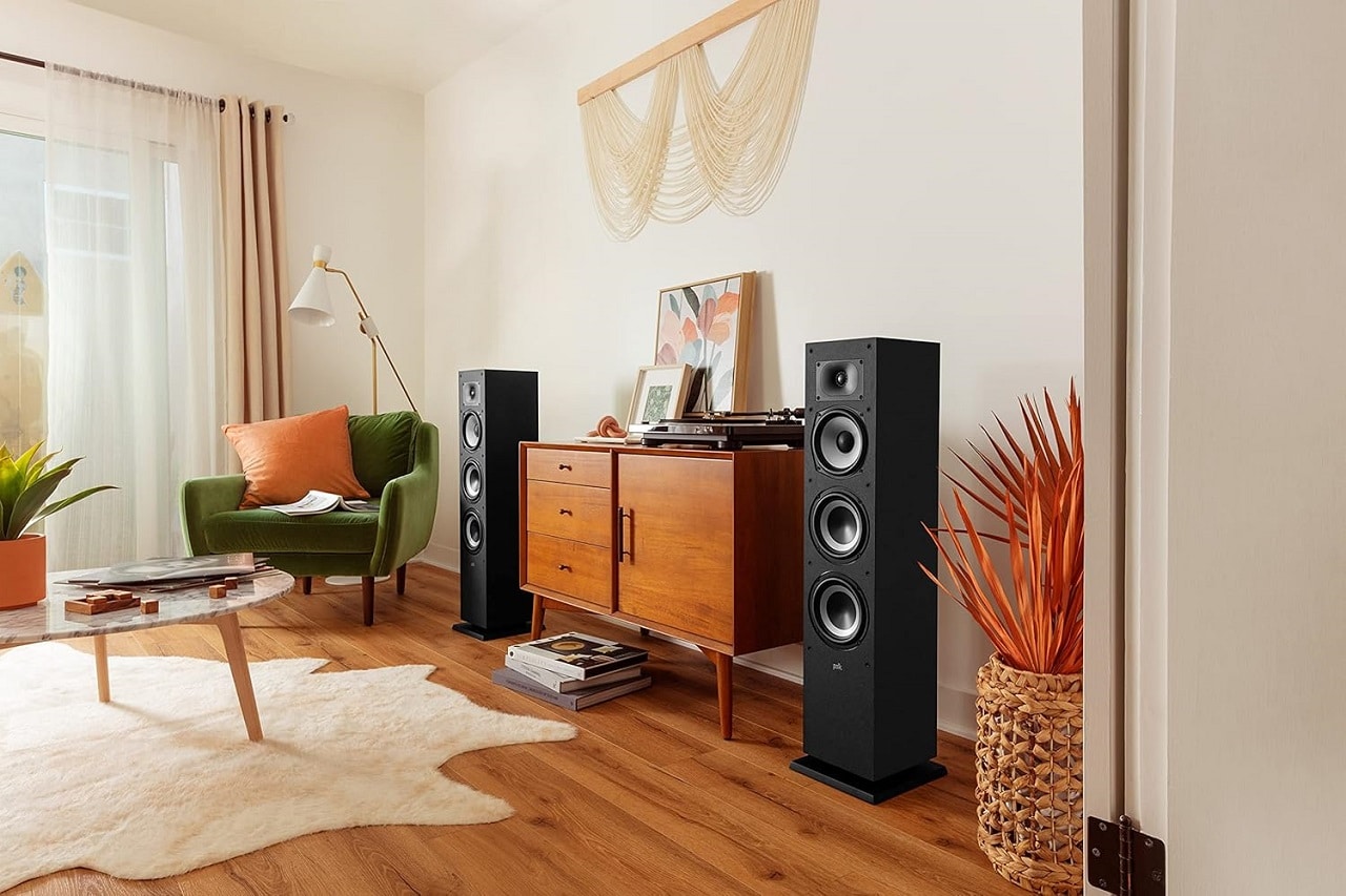 Une paire d'enceintes colonnes noires installées de chaque côté d"un meuble en bois dans un salon