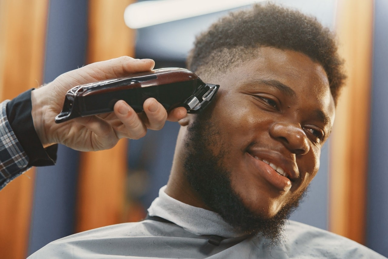 Un homme de type africain en train de se faire couper le cheveux chez le barber qui utilise une tondeuse pour cheveux afro
