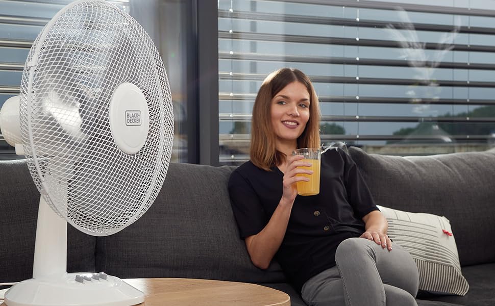 Une femme assise dans son canapé se rafraichit avec son ventilateur de table Black et Decker