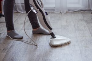 A young woman washes the floor with a modern steam cleaner.
