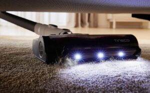 Un aspirateur balai de la marque Tineco qui aspire un tapis sous un lit.