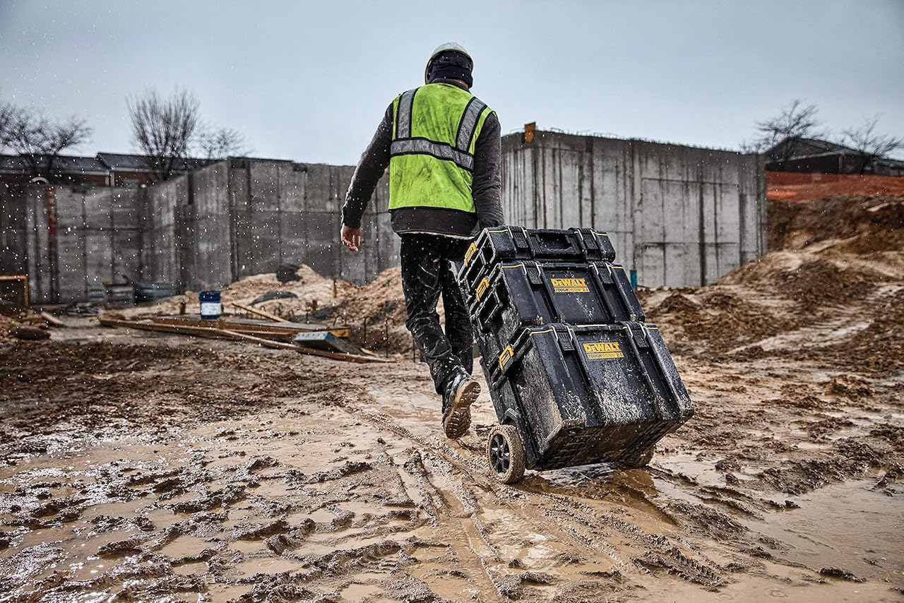 Un homme sur un chantier en train de transporter des coffrets de rangement de la marque DeWalt.