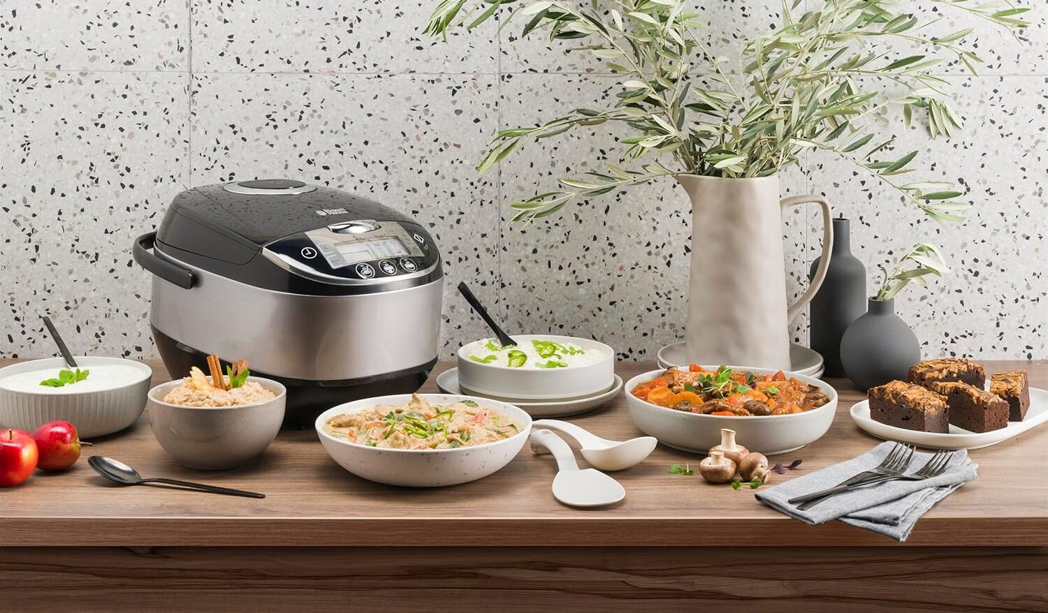 Un autocuiseur de la marque Russell Hobbs posé sur une table de cuisine et entouré de plusieurs plats préparés