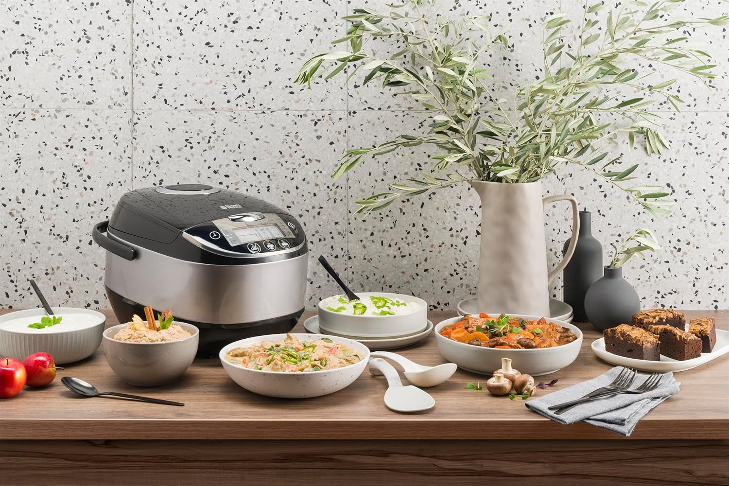 Un autocuiseur de la marque Russell Hobbs posé sur une table de cuisine et entouré de plusieurs plats préparés