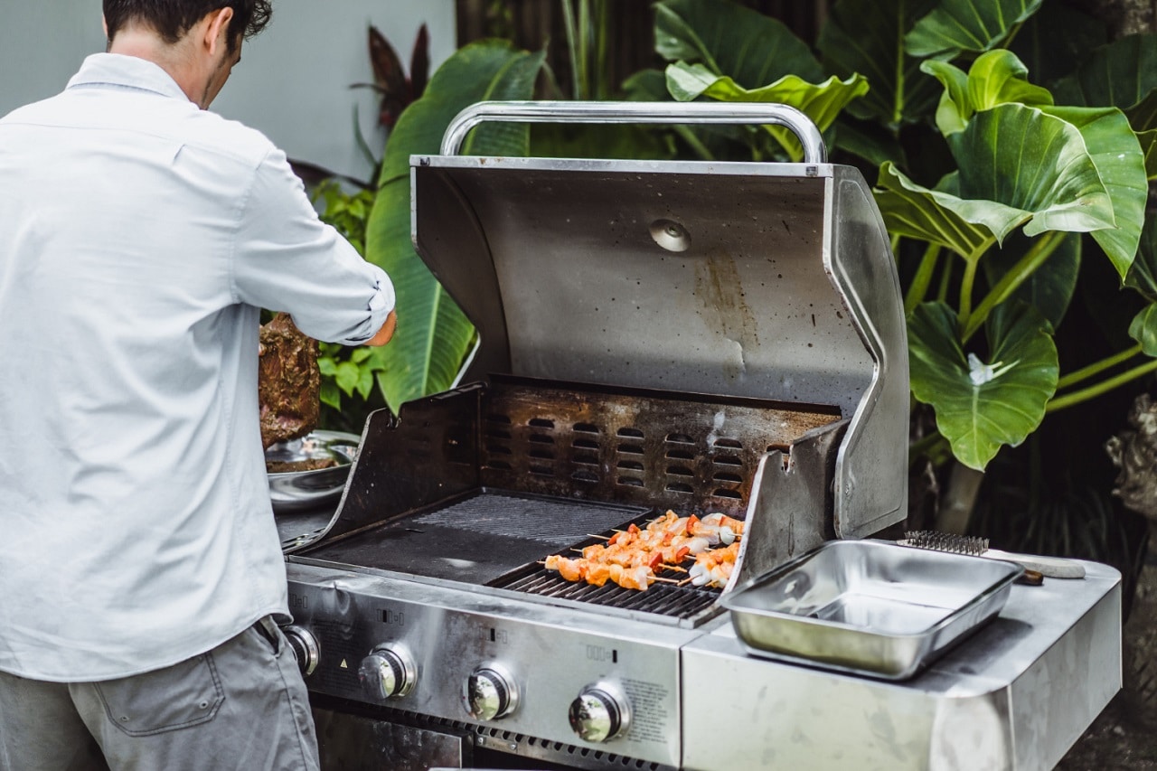 Un homme en chemise blanche est en train de faire cuire de la viande avec un barbecue à gaz