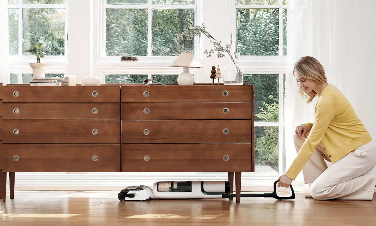 Une femme qui aspire en dessous d'un meuble à l'aide d'un aspirateur Tineco.