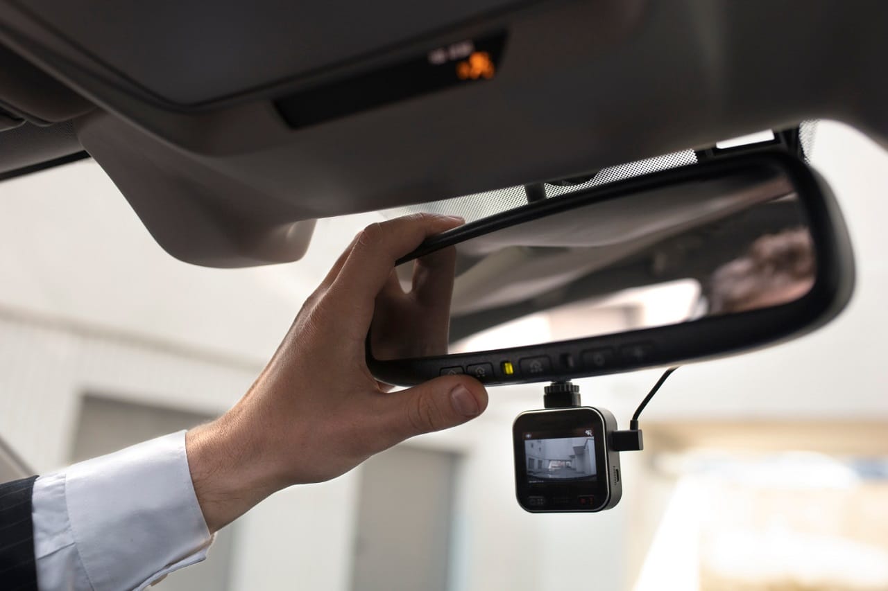 Gros plan sur le rétroviseur intérieur d'une voiture au dessous duquel est installée une dashcam.
