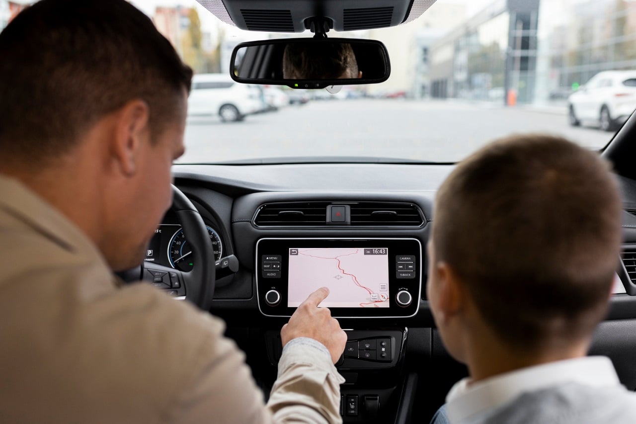 Un père et son jeune fils dans une voiture. Le père fait une recherche sut l'écran du GPS