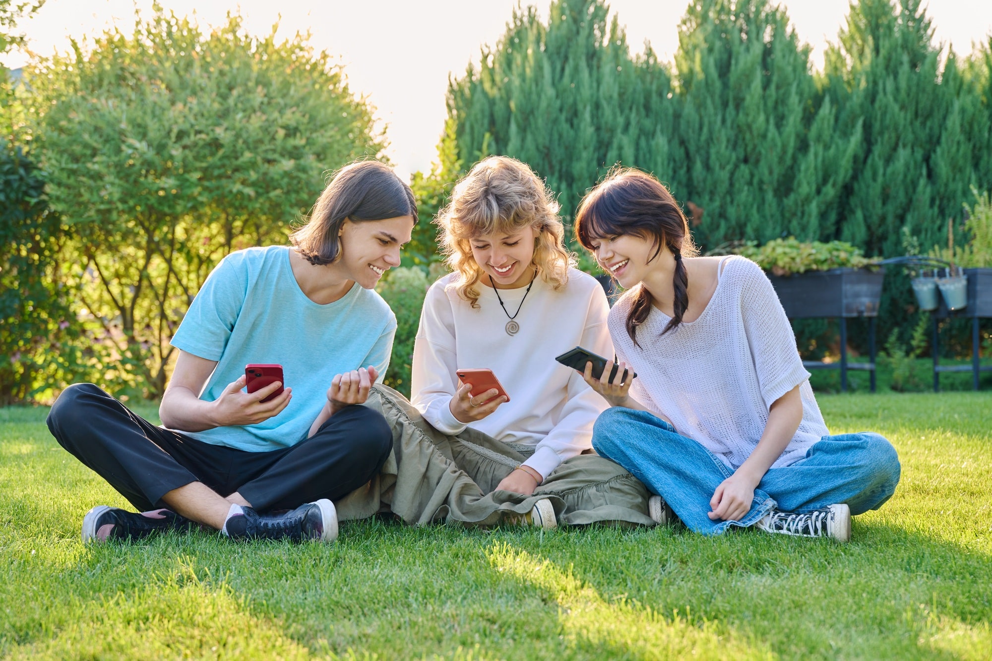 Teenage friends sitting on the grass with smartphones