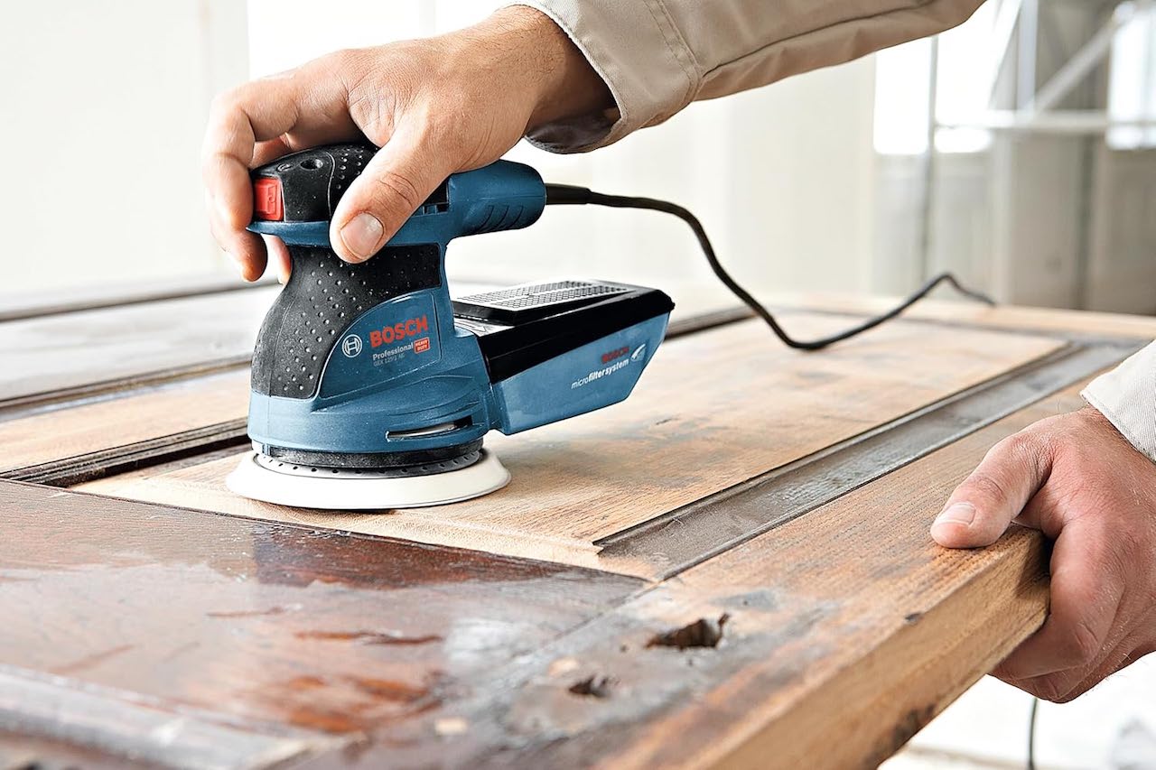 Un homme qui utilise une ponceuse de la marque Bosch.