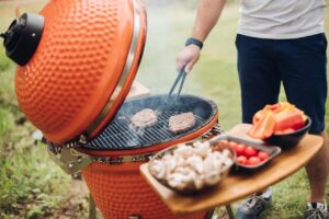 Un homme dont on ne voit pas le visage retourne ses steacks en train de cuire avec son barbecue Kamado orange