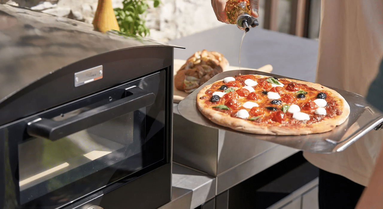 Une personne qui sort une pizza d'un four à pizza électrique.