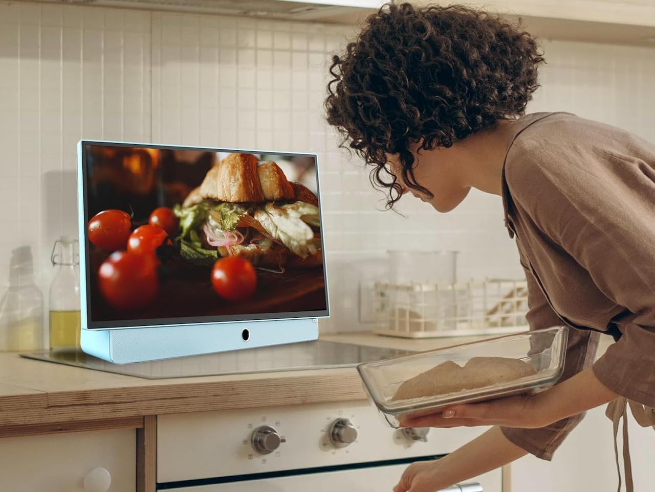 Une femme dans une cuisine qui regarde la télé sur une TV portable.