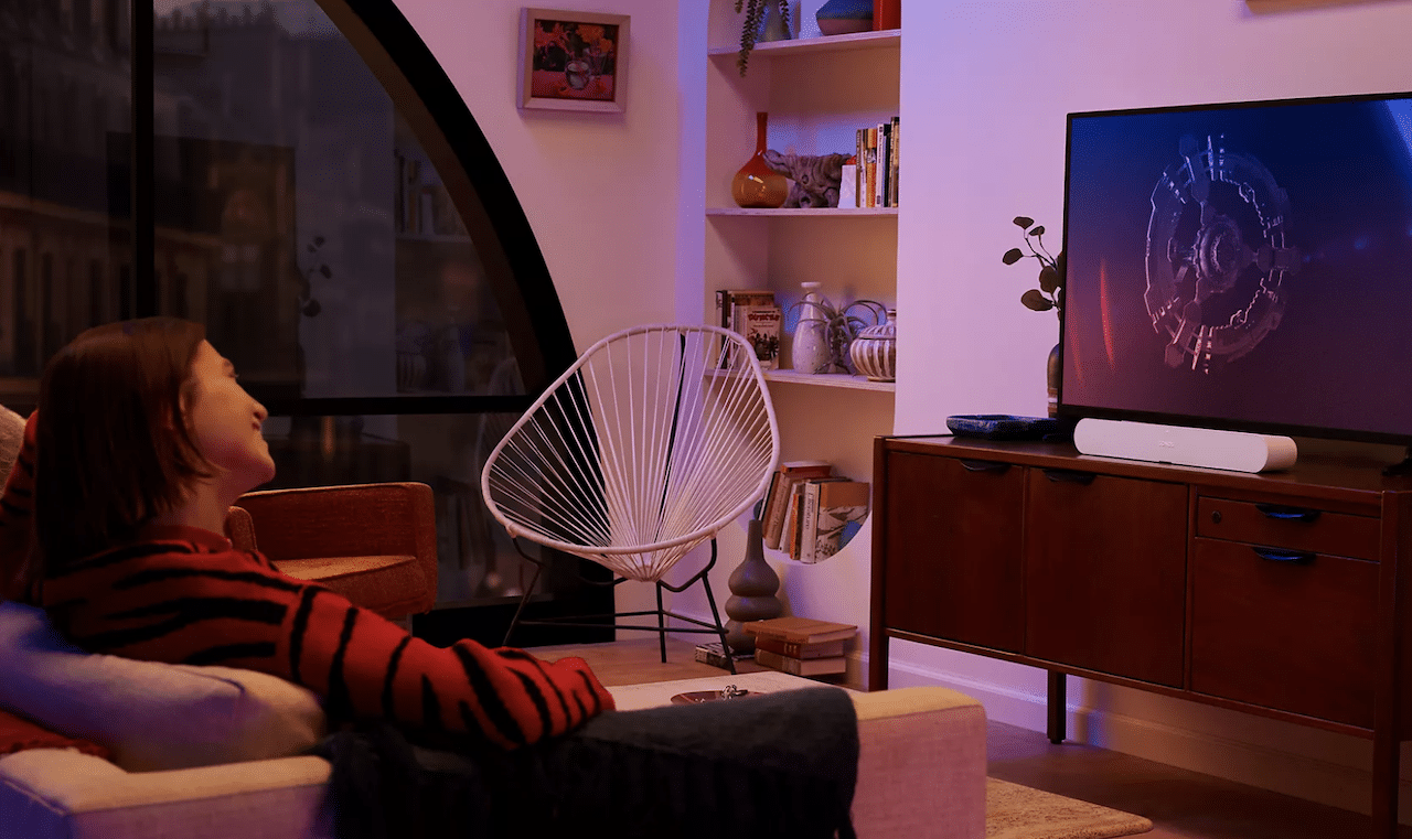 Une femme qui profite d'une barre de son Sonos dans son salon.
