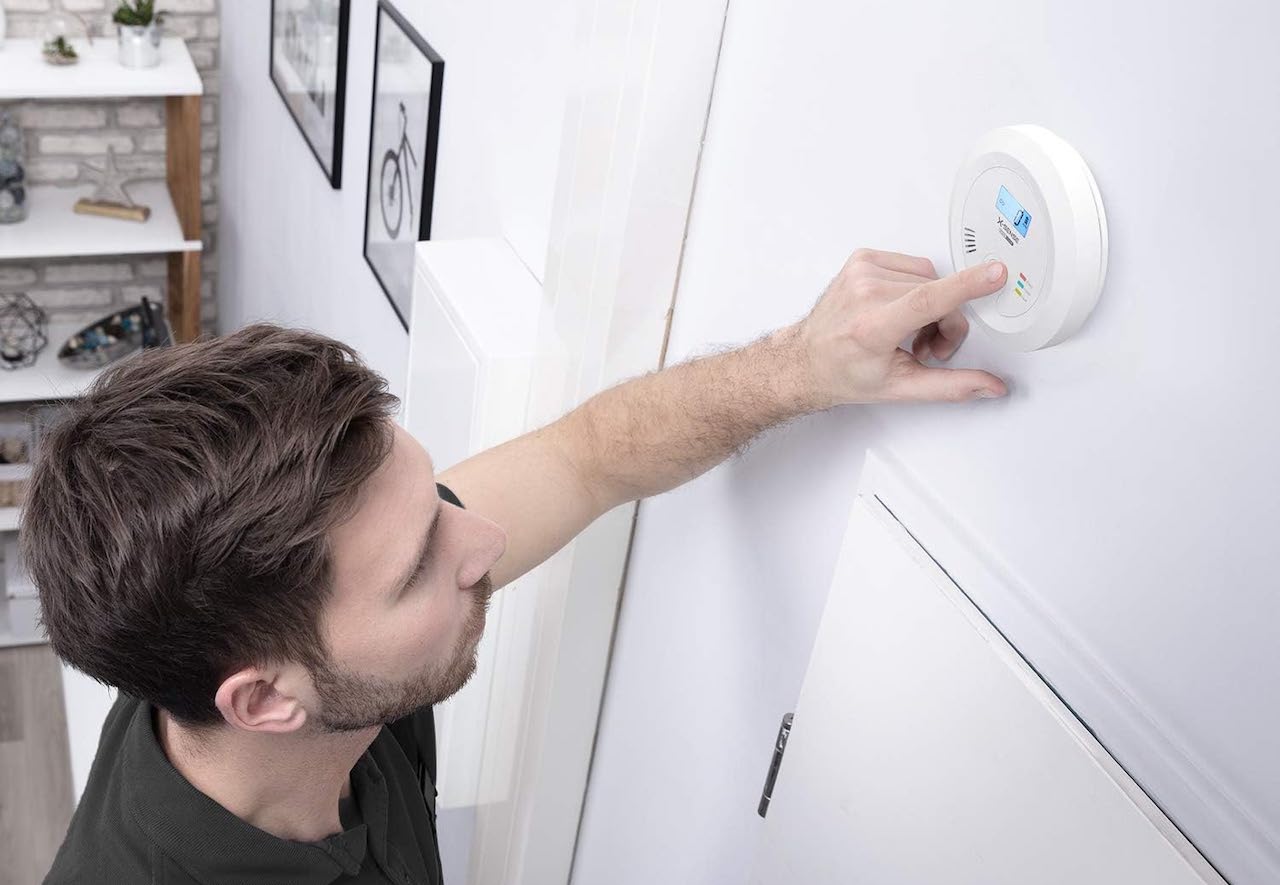 Un homme qui configure un détecteur de monoxyde de carbone sur un mur.