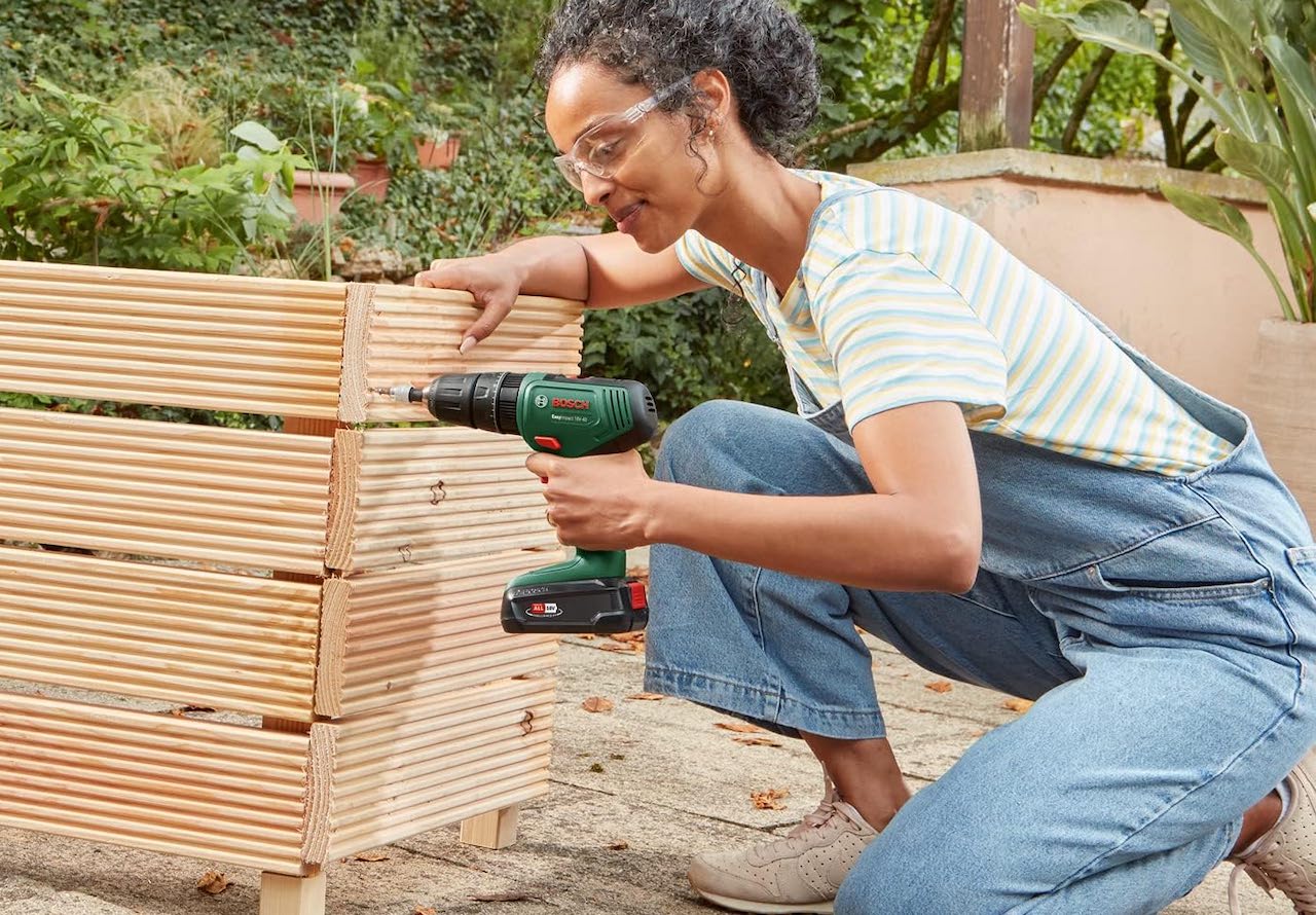 Une femme qui utilise une perceuse-visseuse dans son jardin.