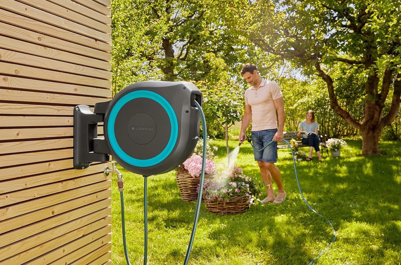 Un homme qui arrose sa pelouse à l'aide d'un dévidoir de la marque Gardena.