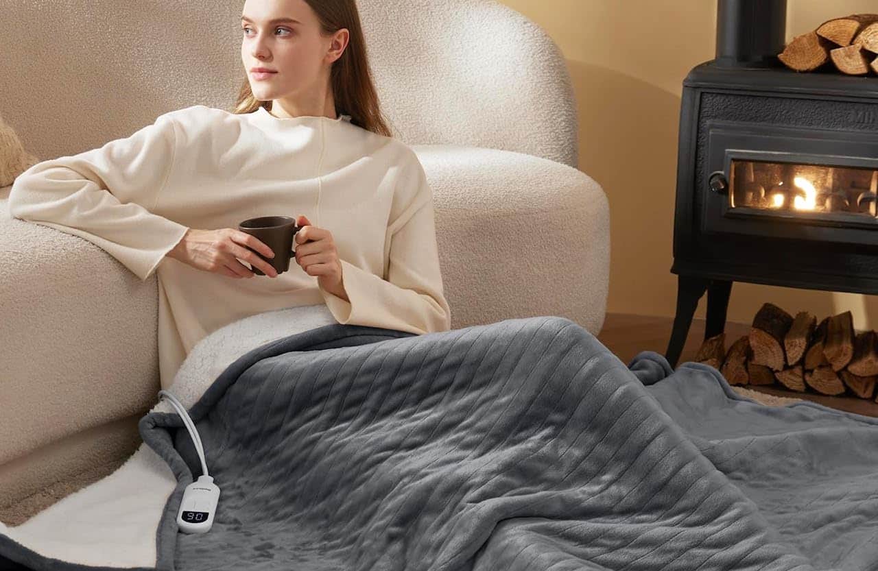 Une femme qui est assise près d'une cheminée avec une couverture chauffante.