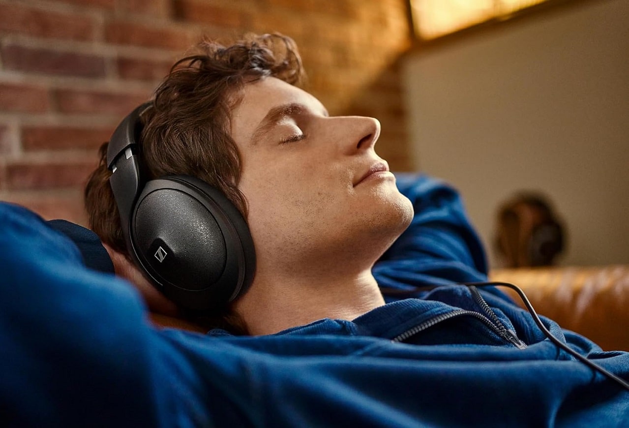 Gros plan sur le visage d'un jeune homme les yeux fermé allongé sur son canapé, écoutant de la musique avec le casque audio Sennheiser HD 620S sur les oreilles