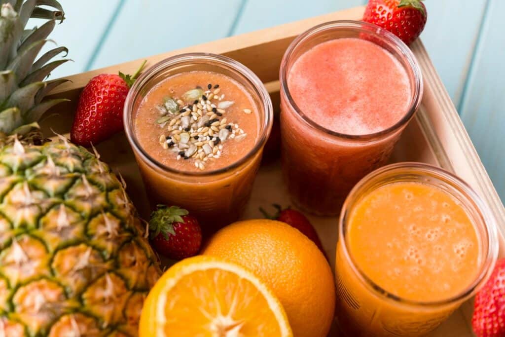 3 grands verres de jus de fruits pressés posés sur un plateau en bois