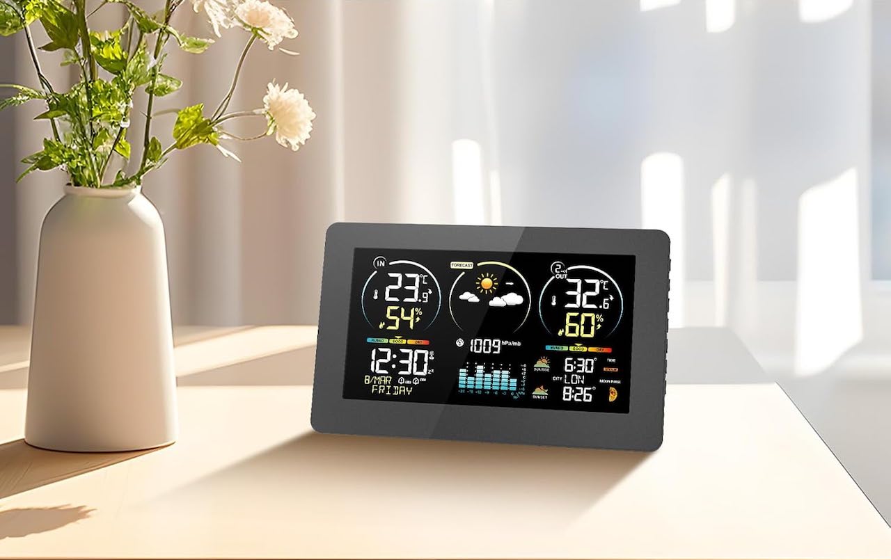 Une station météo posée sur une table près d'un vase avec des fleurs.