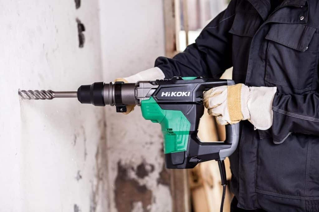 Un homme qui utilise un marteau de forage et de burinage de la marque HiKOKI sur un chantier.