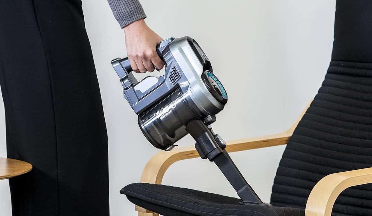 Une femme qui utilise un aspirateur balai sur un canapé.
