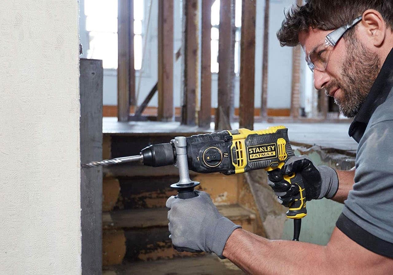 Un homme qui utilise une perceuse à percussion de la marque Stanley sur un chantier.