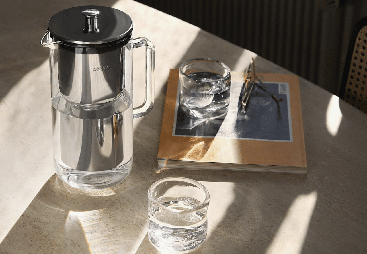 Une carafe filtrante de la marque Aarke posée sur une table à côté des verres design.