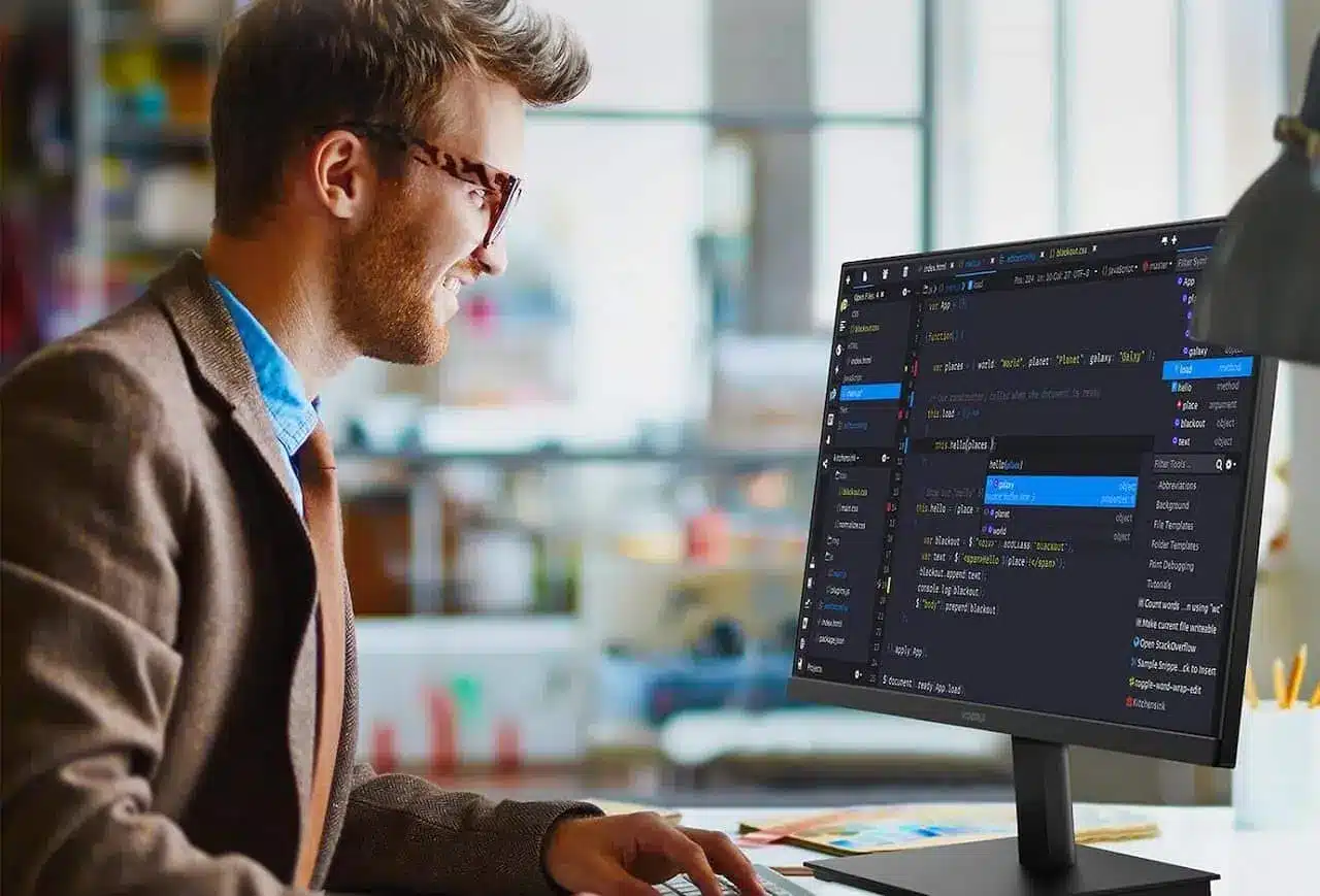 Un homme avec des lunettes et une veste marron est à son bureau devant son écran de PC