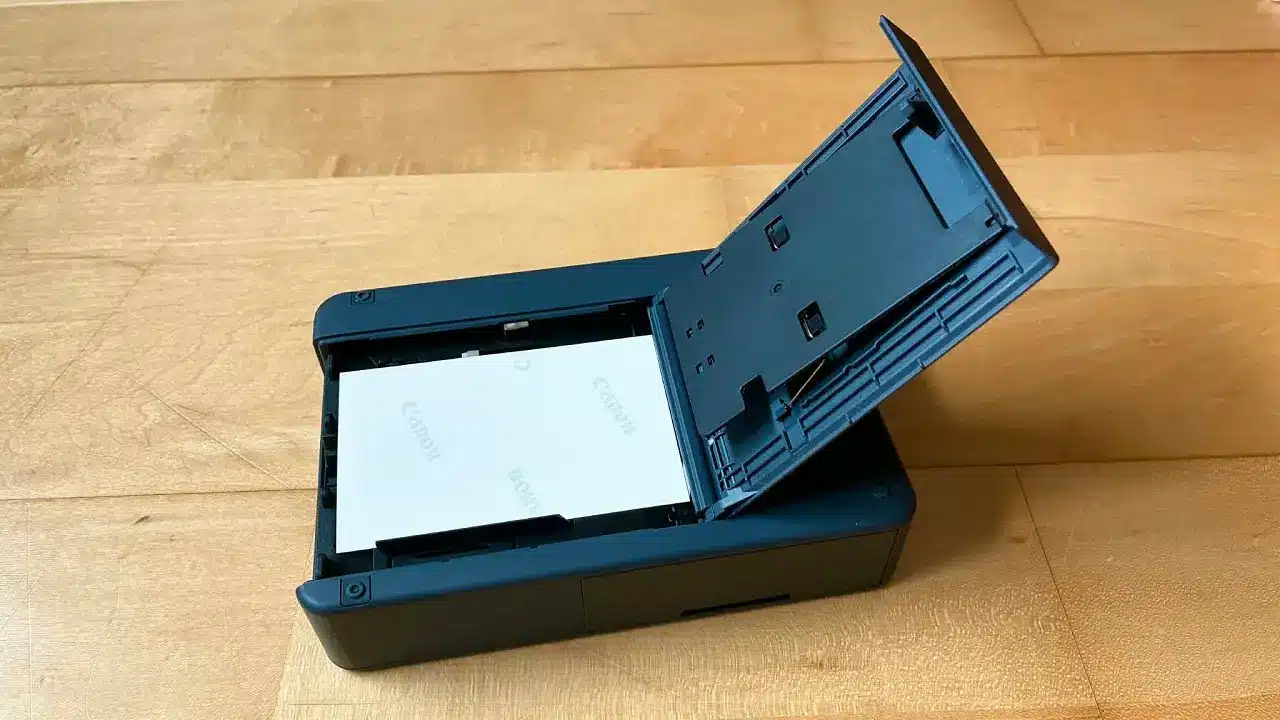 L'imprimante Canon Selphy QX20 avec le capot arrière ouvert laissant voir le chargement du papier photo.