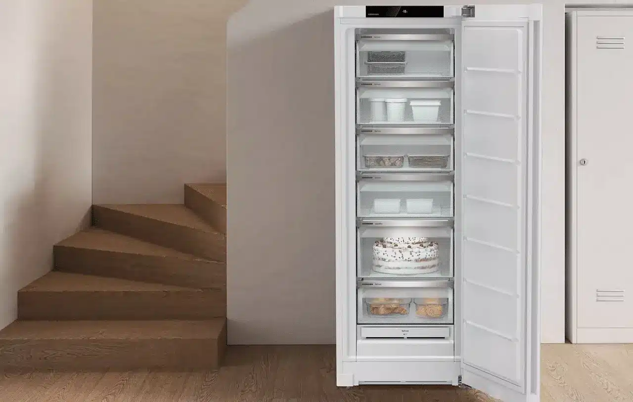 Un congélateur armoire avec sa porte ouverte laissant voir ses tirroirs plein de denrées.