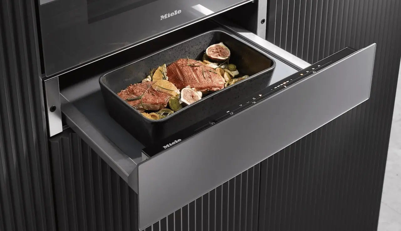 Un tiroir chauffant de la marque Miele encastré dans une colonne de cuisine aux tons noirs avec au dessus un four Miele.