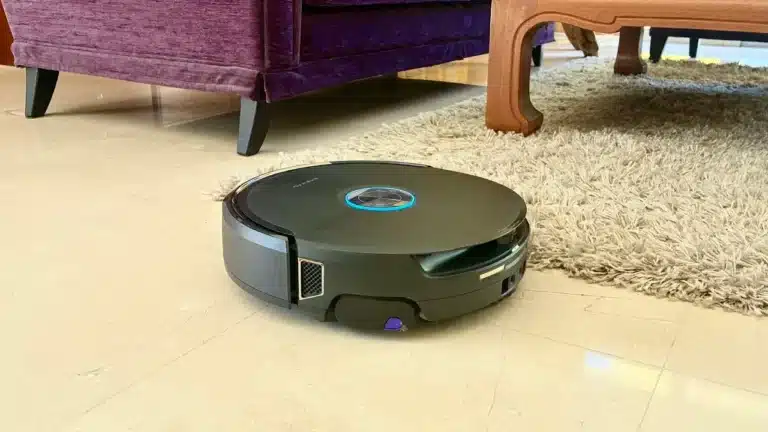 Le robot aspirateur laveur Narwal Flow 2 sur un sol en marbre, à côté d'un tapis à poils longs