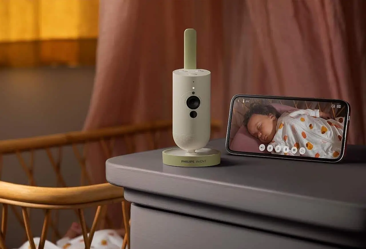 Un babyphone vidéo posé sur la commode d'une chambre d'enfant avec à coté un smartphone sur lequel est affiché l'image du bébé endormi dans son lit.